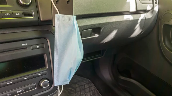 Blue medical mask on a car dashboard. Life in Coronavirus quarantine and virus danger concept