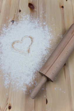 Yuvarlanan iğne ve tahta masaya dökülen beyaz un ve bir kalp çizimi. Pişirme konseptine bayılırım. Sevgililer Günü tatlı pişiriyor.