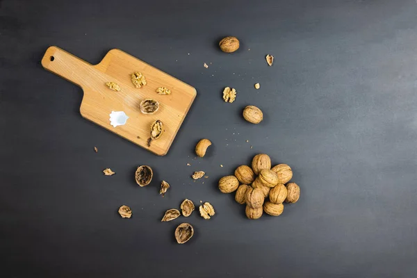 Walnuts on black, dark background, with opening tool on a wooden cutting board. Opening walnuts and taking them out of their shell. Preparation for healthy baking or cooking with nuts