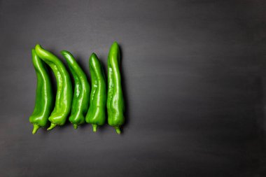 Yatay çizgide koyu siyah arkaplanda bir sürü yeşil biber var. Renkli sebzeler, yemek malzemeleri.