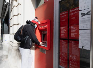 CALDES DE MonTBUI, İSPAN - 31 HAZİRAN 2021: Şapka ve koruyucu yüz maskesi takan genç adam, Katalonya 'daki Santander Bankası' nın ATM 'sini kullanıyor.