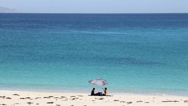 Cortes Denizi kıyısında bir plaj şemsiyesi altında iki siluet, Punta Arena de La Ventana, BCS, Meksika - 1 Mayıs 2021