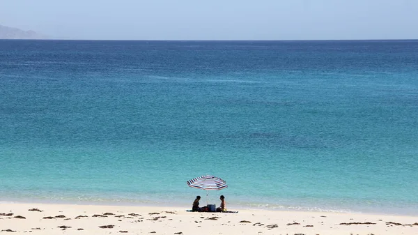 Cortes Denizi kıyısında bir plaj şemsiyesi altında iki siluet, Punta Arena de La Ventana, BCS, Meksika - 1 Mayıs 2021