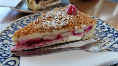 Süslü mavi ve beyaz tabakta bir dilim ahududu peynirli kek.