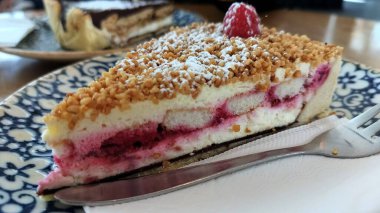 Süslü mavi ve beyaz tabakta bir dilim ahududu peynirli kek.