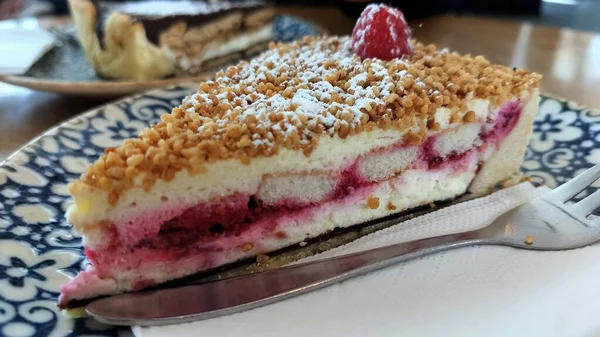 Süslü mavi ve beyaz tabakta bir dilim ahududu peynirli kek.