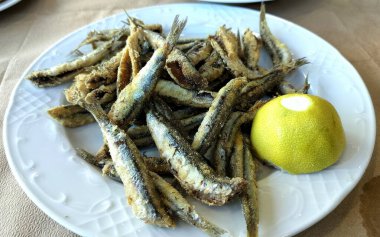 Küçük, çıtır çıtır, kızarmış sardalya. Yarım limonla süslenmiş beyaz bir börek.
