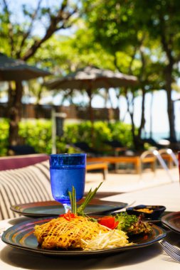 Geleneksel Thai Thai eriştesi. Kızarmış pirinç şehriyesini, fasulye filizi ve havuz başındaki restoranda yer fıstığı ile servis edilen tabakta yumurtalı dürüm ile karıştırın..