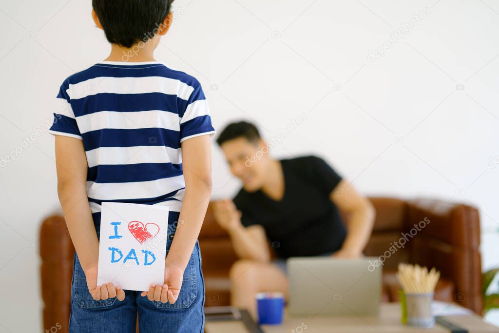 gift card in hand of kid hiding behind want to make surprise giving to father at home. concept of father day and father and son relationship. selective focused