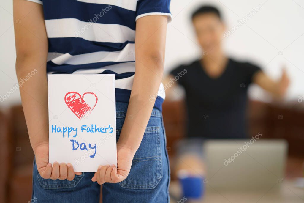 gift card in hand of kid hiding behind want to make surprise giving to father at home. concept of father day and father and son relationship. selective focused