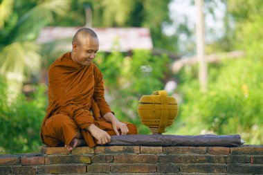 Tapınaktaki eski tuğla duvarda oturan keşiş uzun saplı şemsiyeli ve sadaka kaseli Budist keşiş.