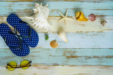 Yaz tatili arka planında terlikler güneş gözlüğü deniz kabuğu ve mavi ahşap tahtada yıldız balığı. Yaz tatili konsepti adaya ya da deniz kıyısına seyahat