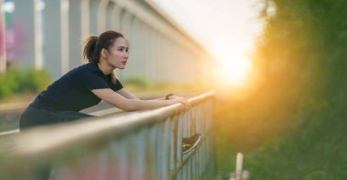 Spor arka planında Asyalı genç atletik kadın parıltısı sabah parkın yanındaki tren yolu boyunca koştuktan sonra rahatlıyor ve bacak esnetiyordu.