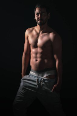 Kaslı genç model adamın koyu arkaplanda portresi. Seksi çıplak gövde, karın kasları. Kas konsepti olan erkek model..