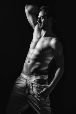 Siyah beyaz bir portre ve kaslı genç bir modelin koyu arkaplanı. Seksi çıplak gövde, karın kasları. Kas konsepti olan erkek model..