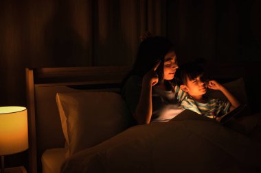 Asyalı anne ve kızı birlikte iyi vakit geçiriyorlar anne uyumadan önce çocuk için masallar okuyor. Anne-kız ilişkisi kavramı