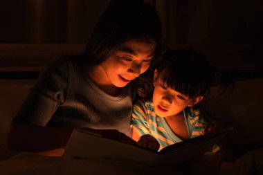 Asyalı anne ve kızı birlikte iyi vakit geçiriyorlar anne uyumadan önce çocuk için masallar okuyor. Anne-kız ilişkisi kavramı