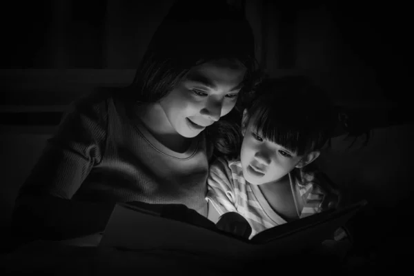 asian mom and daughter having goodtime together mom reading bedtime stories fairytale for daughter on bed before getting to sleep. concept of mother and daughter relationship