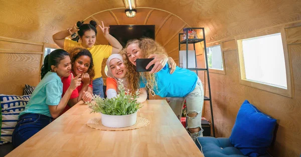diverse multicultural women friends get together and taking selfie together in recreation and meeting room in RV vehicle during travelling in carvan