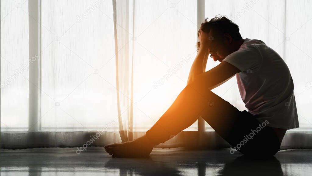 silhouette drametic portrait of caucasian man sitting alone by window at home looking sorrow with desperate feeing and depressed from unemployment with sun flare