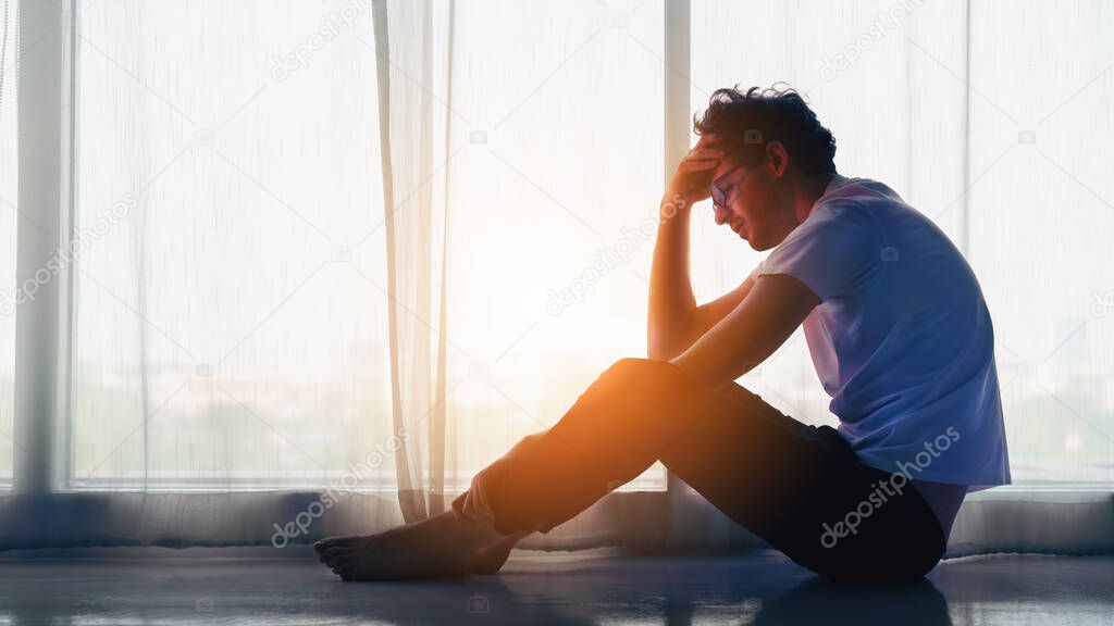 dramatic portrait of caucasian man sitting alone by window at home looking sorrow with desperate feeing and depressed from unemployment with sun flare