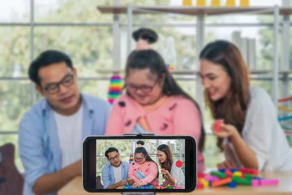 asian down syndrome teenage girl with father and mother as blogger and vlogger for down syndrome parent broadcasting live online together when playing education toy