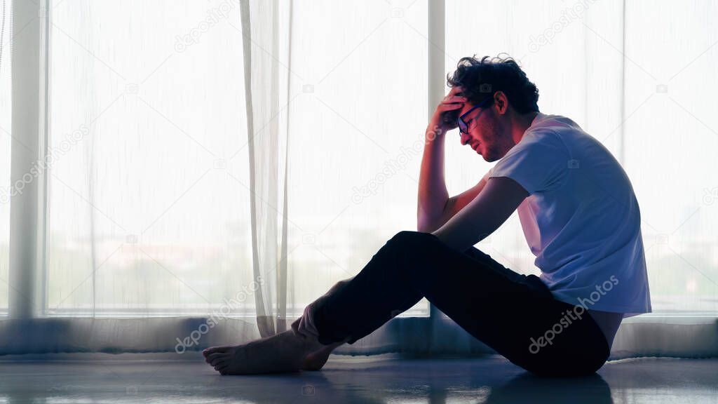 dramatic portrait of caucasian man sitting alone by window at home looking sorrow with desperate feeing and depressed from unemployment