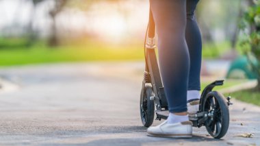 Parkta kaldırımda scooter 'la gezen bir kadının spor ve egzersiz geçmişi.