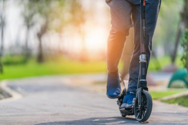 Açık havada egzersiz yapmak ve arka planda egzersiz yapmak. Otoparkta parktaki kaldırımda uçan scooter 'a binen ve güneş ışığıyla parlayan adam.