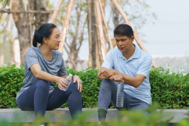 Parkta egzersiz yaptıktan sonra su içen Asyalı çift.