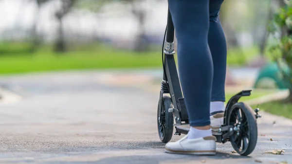 outdoors workout and exercise background of woman ridding on kick scooter on pavement in park