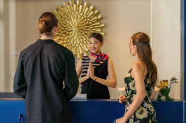 Otel resepsiyonistine hoş geldiniz. Tayland wai 'li beyaz bir çift ve otel resepsiyonuna vardıktan sonra gülümseyin.