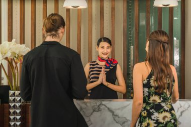 Otel resepsiyonistine hoş geldiniz. Tayland wai 'li beyaz bir çift ve otel resepsiyonuna vardıktan sonra gülümseyin.