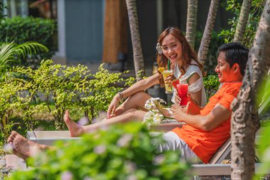 Asyalı çift yaz tatilinde tatil köyünde ve havuz başında otel bahçesinde iyi vakit geçiriyorlar.