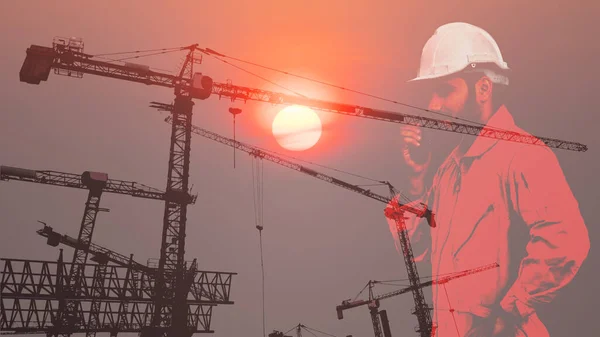 double exposure silhouette civil engineering background of civil engineer in uniform with hard hat using communication radio overlay with tower crane at urban construction site on sunset background