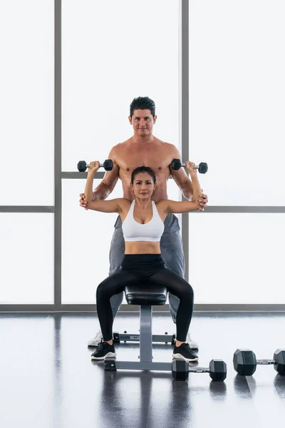 caucasian male gym trainer coaching and help asian athletic woman workout with dumbbell weight lifting for bodybuilding in gym and fitness club