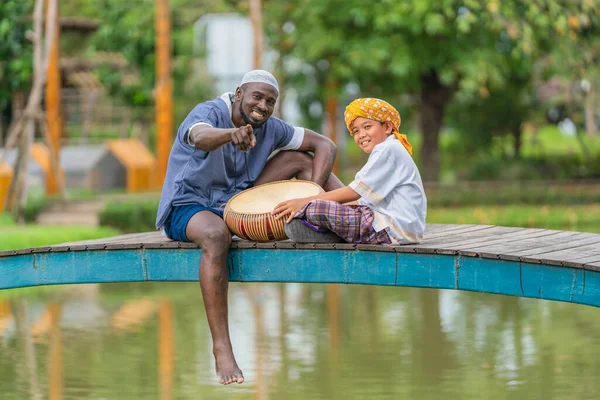 african muslim man and asian muslim boy having fun enjoying playing musilim rabana or kompang drum together after ramadan or hari raya aidilfitri festival celebration