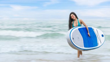 Yaz tatilinde sörf yaptıktan sonra sörf tahtasıyla sahilden denize yürüyen Asyalı güzel bir sörfçü. Plajda yaz tatili aktivitesi kavramı