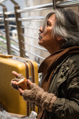 Asyalı zavallı evsiz dilenci yol kenarında oturmuş, elinde ekmek tutuyordu. Yoksulluk ve evsiz insanların sosyal sorunları