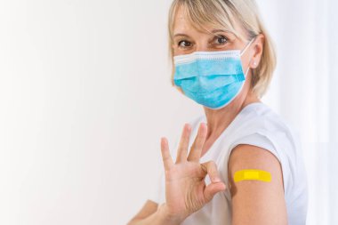 Coronavirus covid-19 aşısı enjekte edildikten sonra kolunu gösteren beyaz bir kadının omzuna yapışkan bir bandaj bandı yerleştirilmiş.