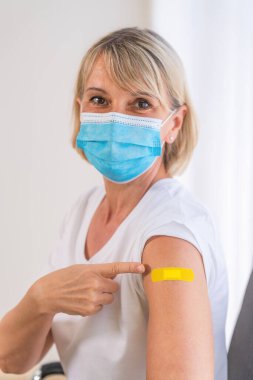 Coronavirus covid-19 aşısı enjekte edildikten sonra kolunu gösteren beyaz bir kadının omzuna yapışkan bir bandaj bandı yerleştirilmiş.