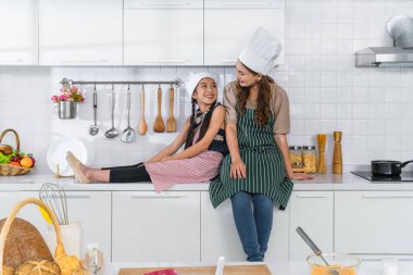 Asyalı anne ve küçük kızı evde birlikte yemek pişirdikten sonra mutfakta oturuyorlar.