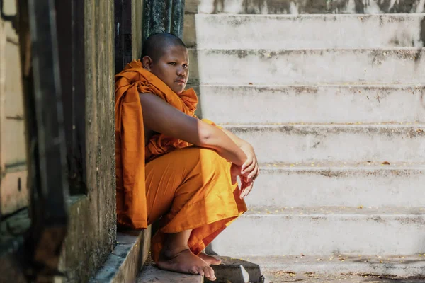 buddhist novice monk in orange robe sitting at door in buddist temple