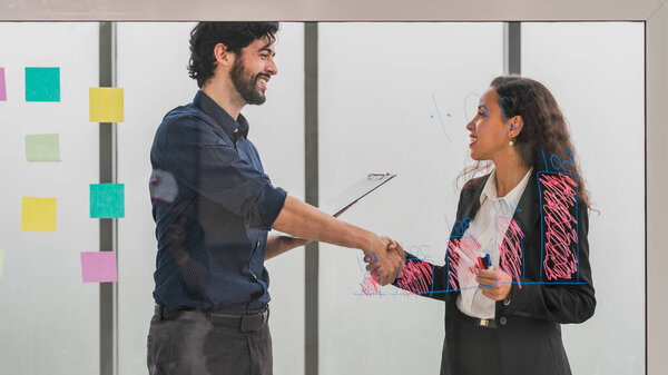 Два успешных бизнесмена, пожимающих друг другу руки после мозгового штурма, и команда, обсуждающая совместное планирование в бизнес-офисе