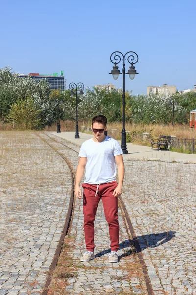 Male teenager standing in a park and wearing sunglasses in sweat — Stock Photo, Image