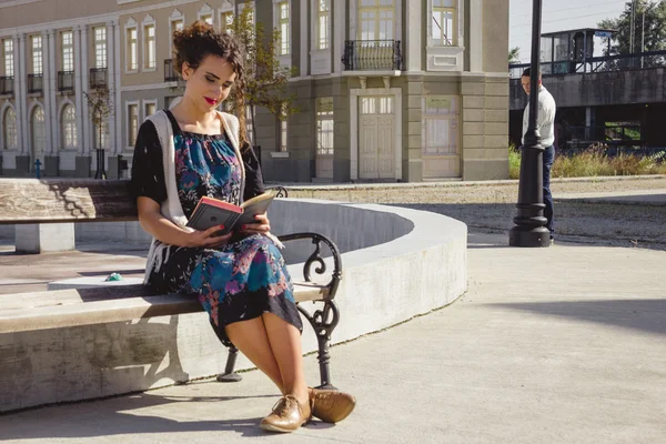 Girl reading book on bench in town while  man is stocking  in th — Stock Photo, Image