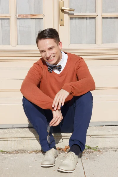 Handsome man in sweater sitting on steps in front of house and p — Stock Photo, Image