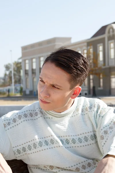 Handsome man posing in white sweater and siting on bench in town — Stock Photo, Image