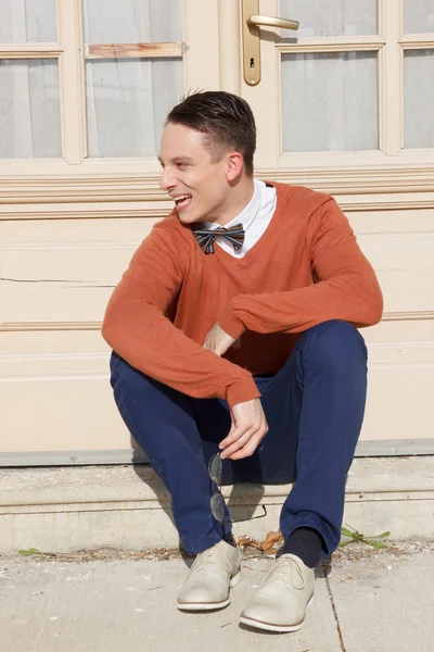 Happy young man in sweater sitting on steps in front of house — Stock Photo, Image