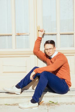 serious handsome man with glasses and sweater sitting on steps i clipart